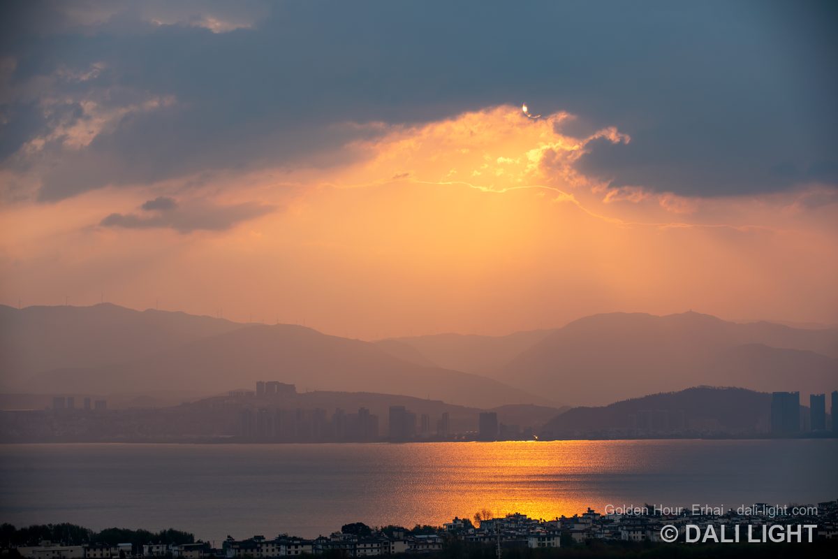 Golden sunset over Erhai lake with layered mountains and village rooftops, Dali